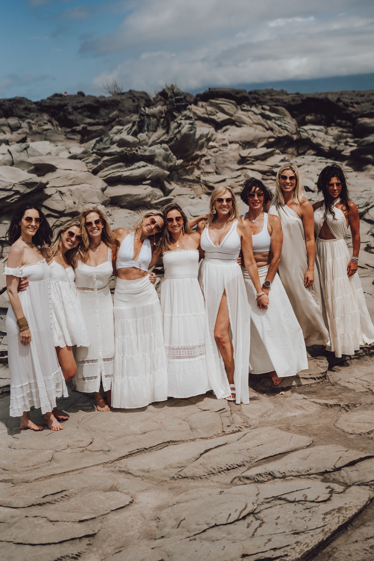 Women in white dresses on rocks by the ocean in Maui