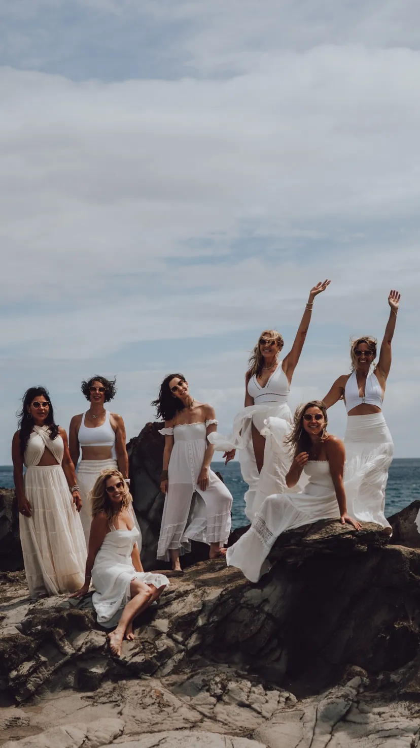 Women in white gathered on rocks by the ocean