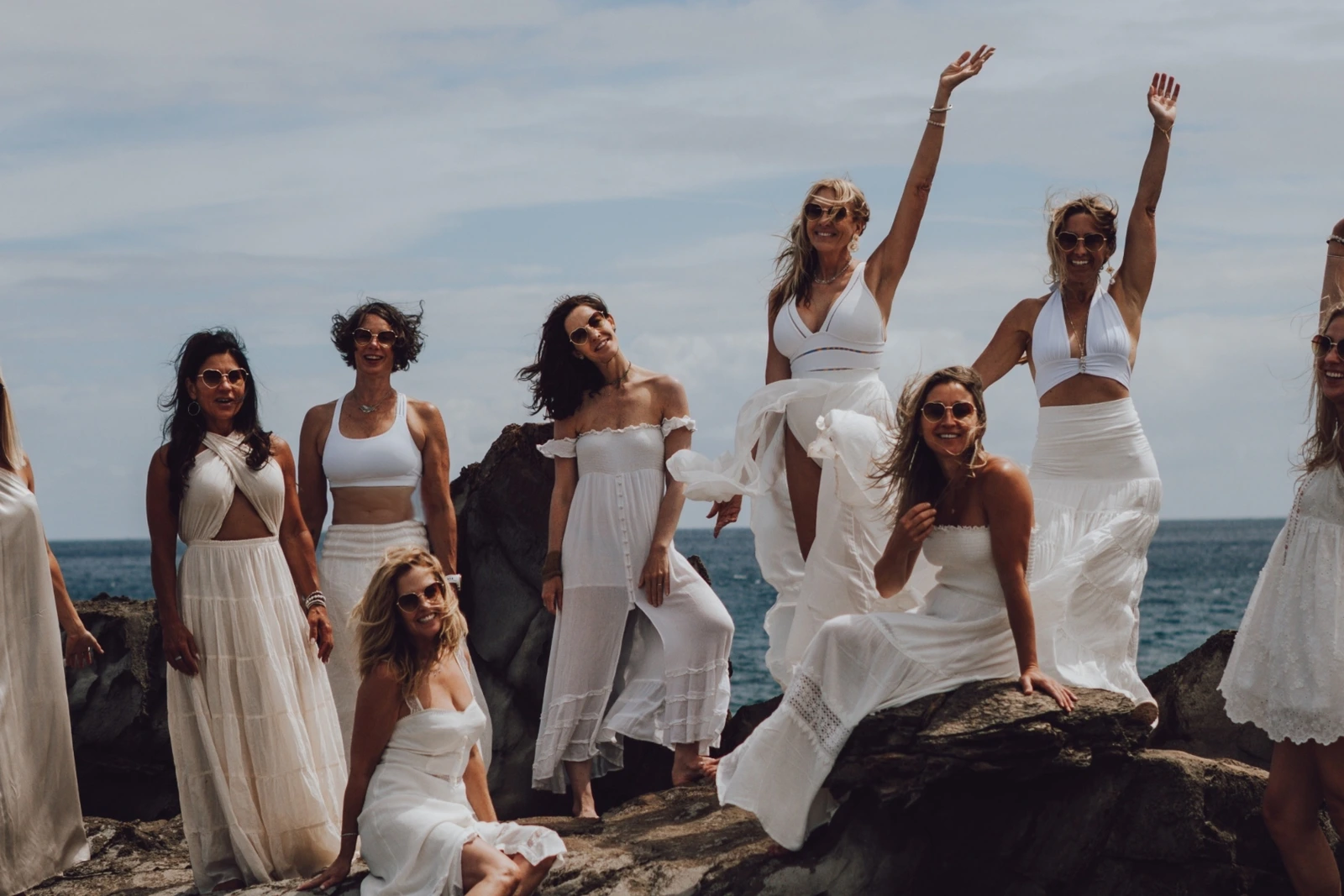 Women in white gathered on rocks by the ocean