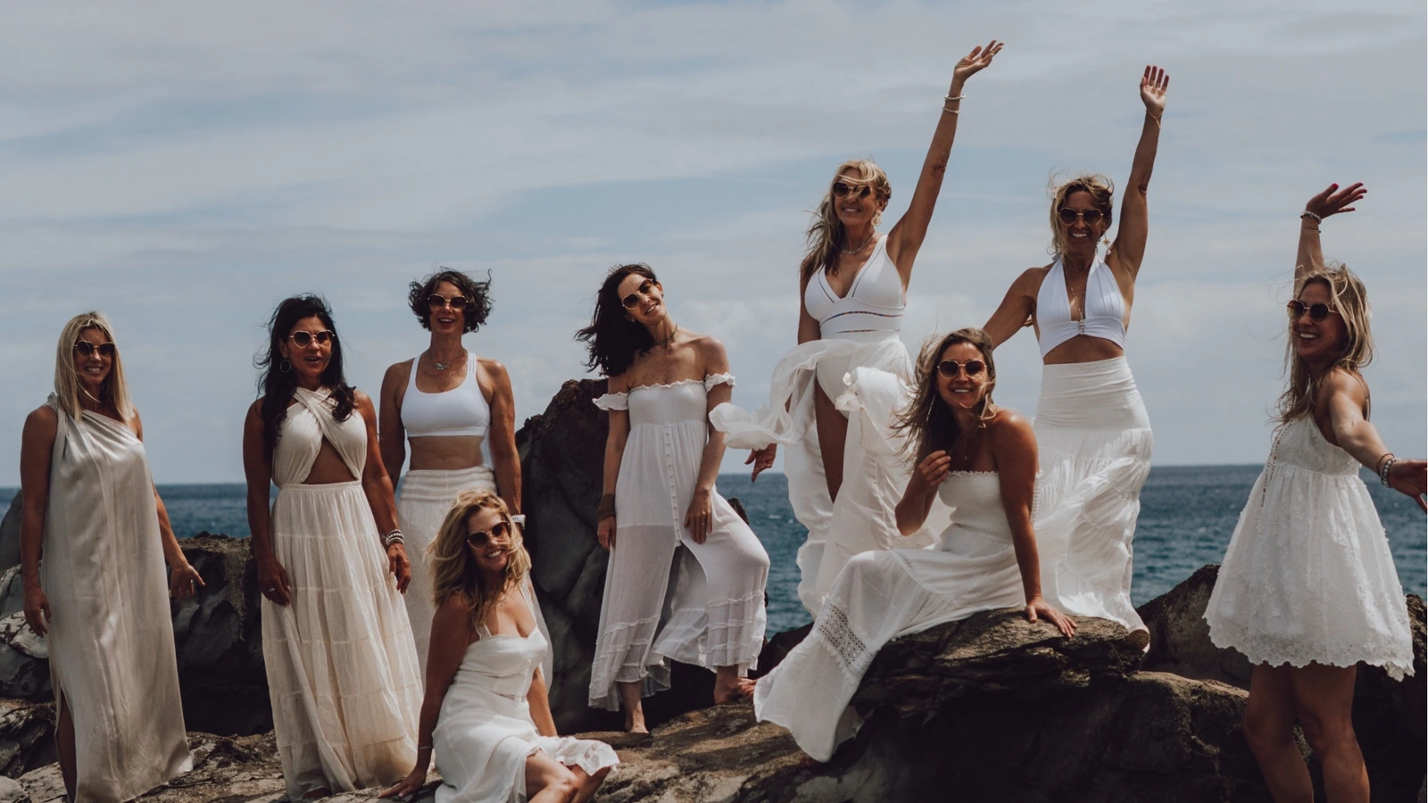 Women in white gathered on rocks by the ocean
