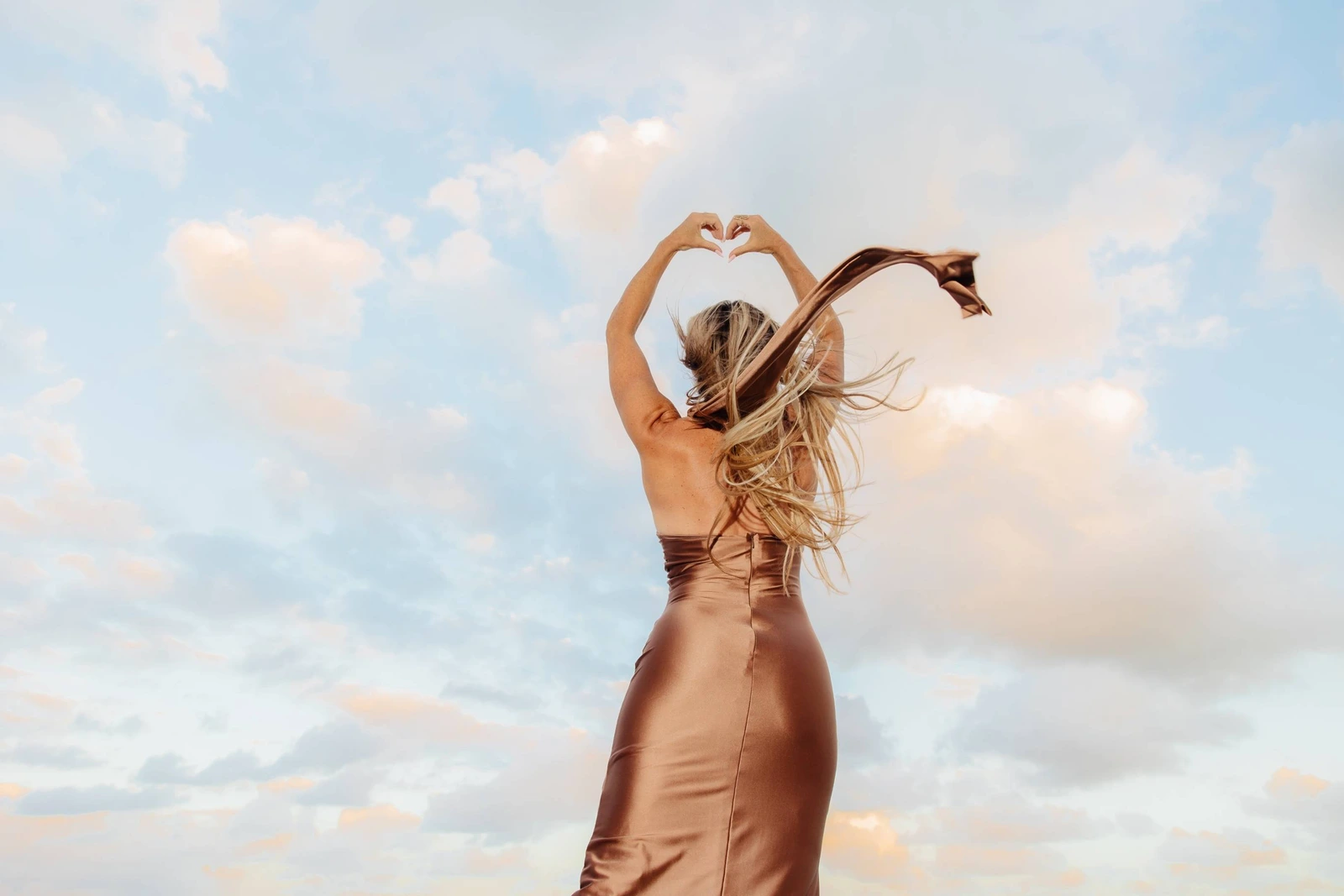 Vanessa with arms raised making a heart shape against the sky